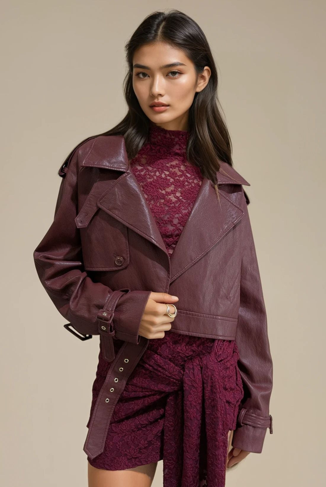 Woman wearing a burgundy trench coat over a matching outfit on a beige background