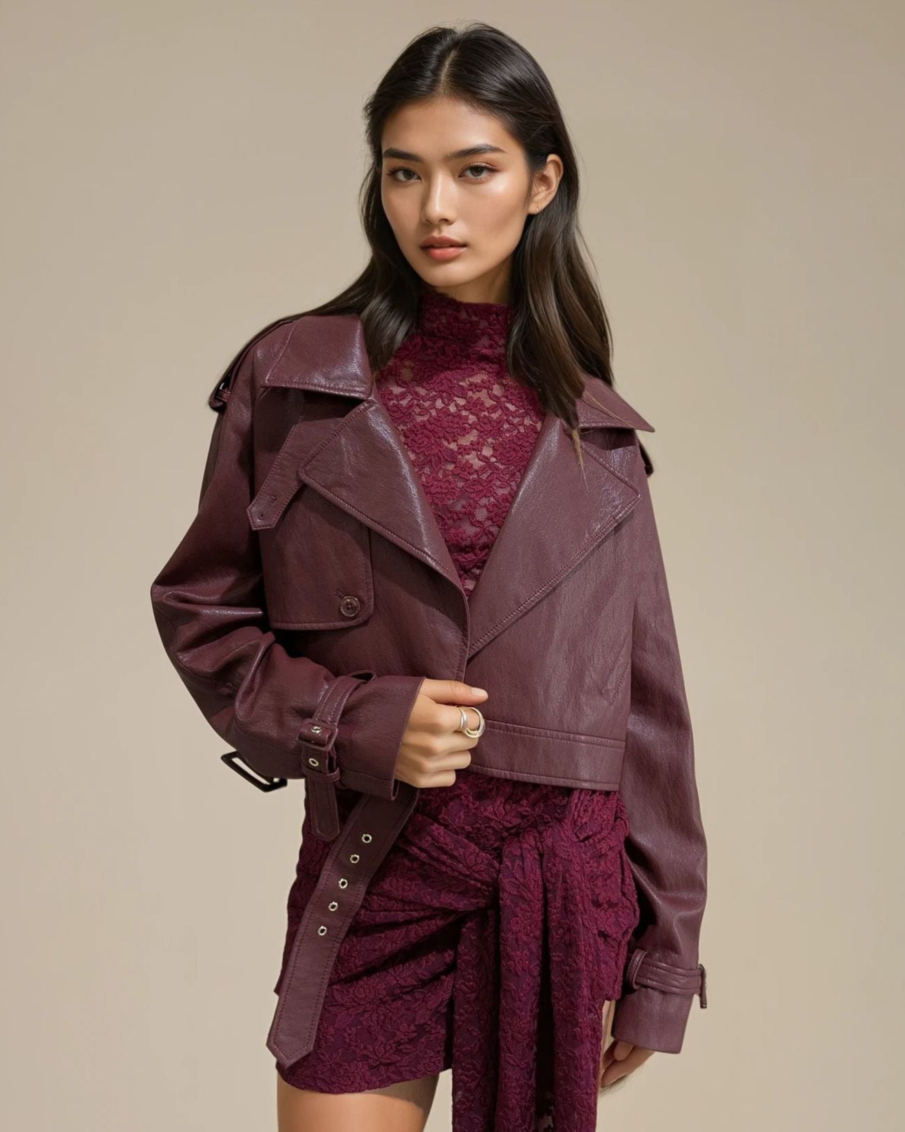 Woman wearing a burgundy trench coat over a matching outfit on a beige background